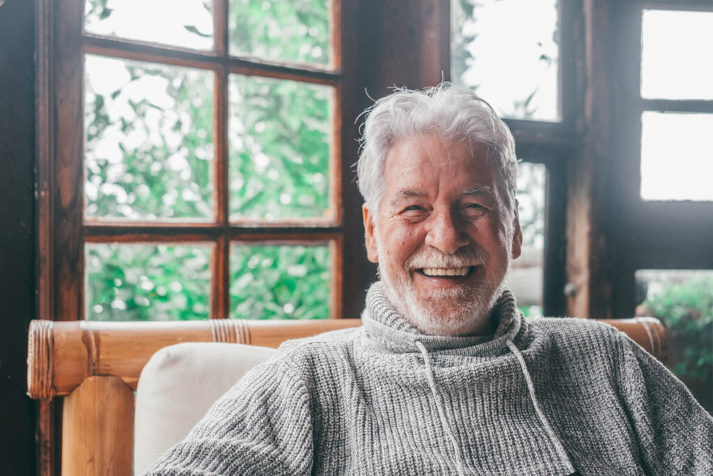 Portrait of old man smiling and looking at the camera sitting on the sofa from home. Closeup male person senior cheerful indoor.