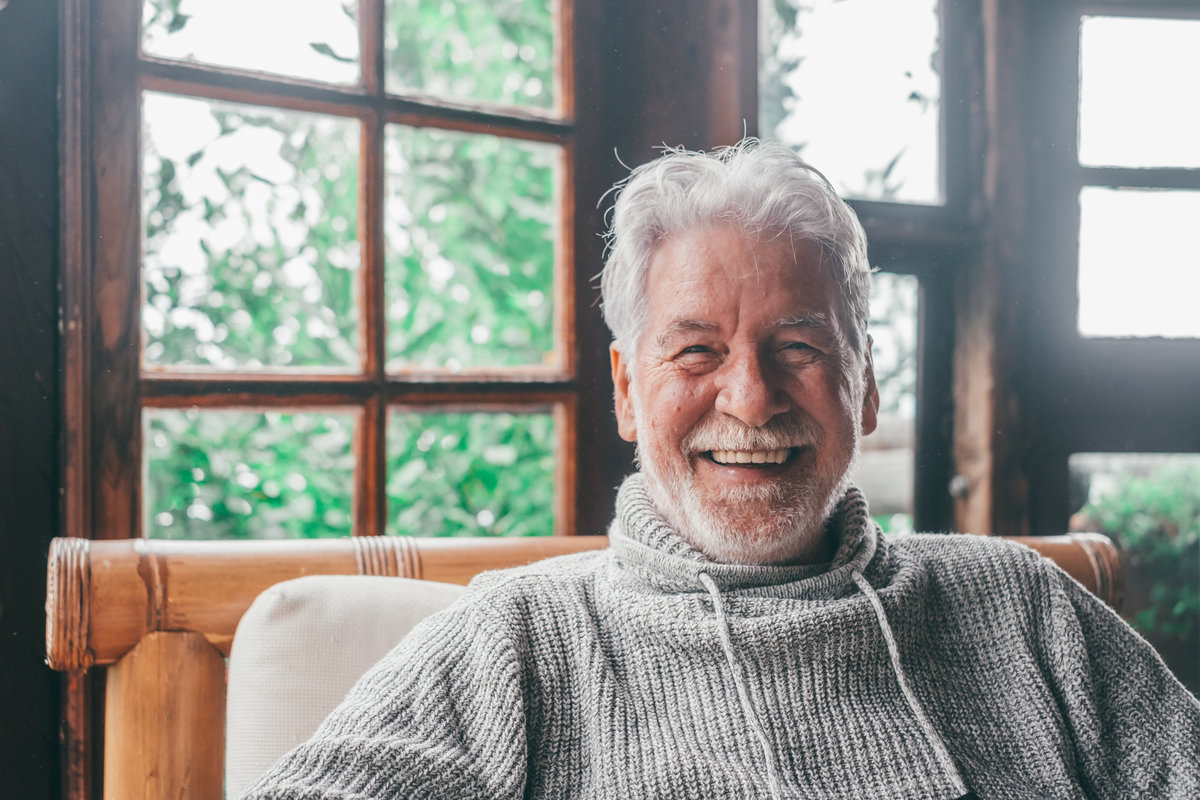 Portrait of old man smiling and looking at the camera sitting on the sofa from home. Closeup male person senior cheerful indoor.