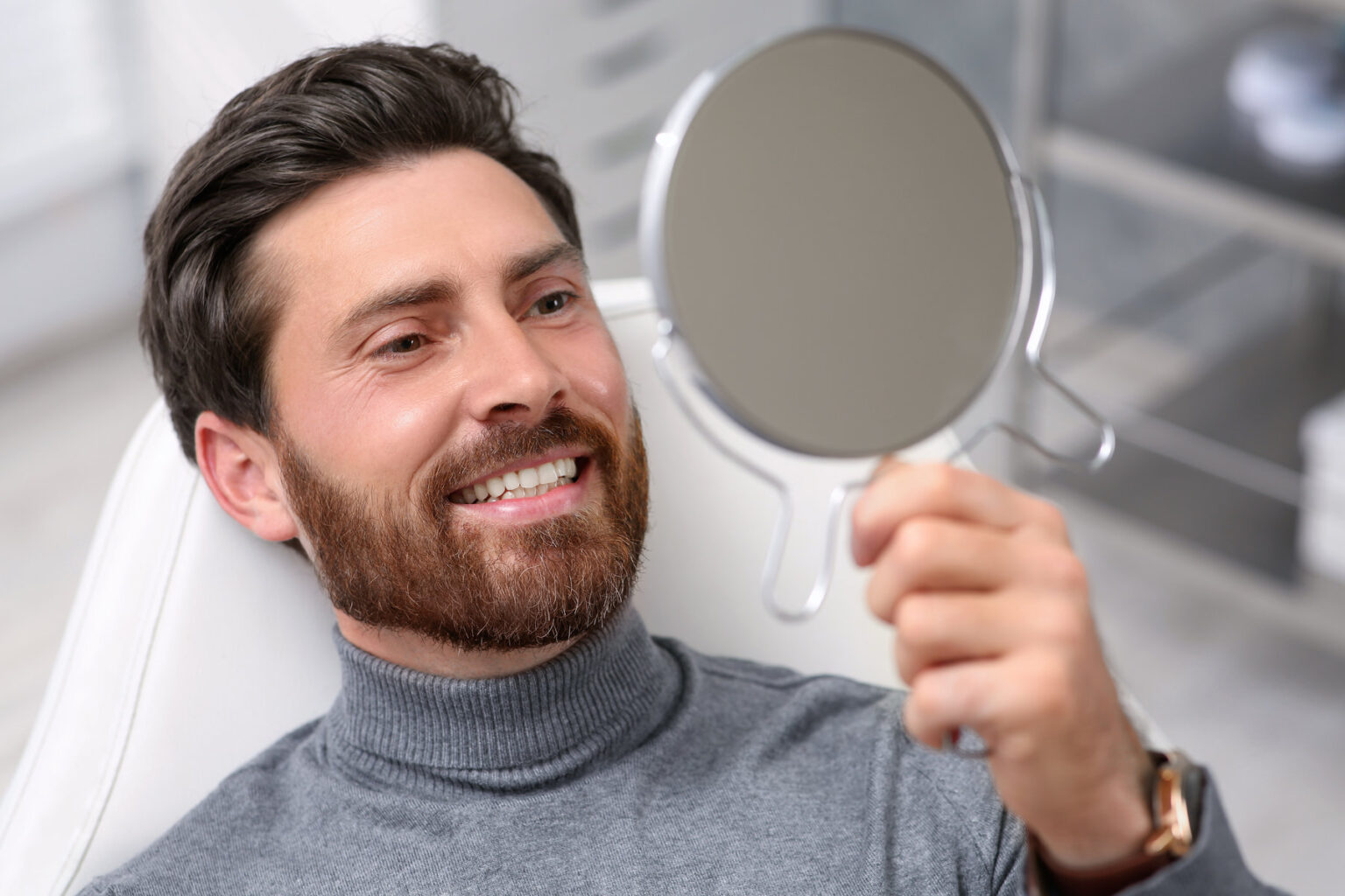Man looking at his new dental implants in mirror indoors