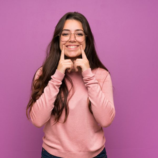 Teenager girl over purple wall smiling with a happy and pleasant expression