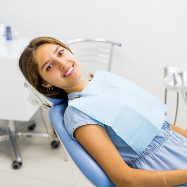 Young woman in blue jeans dress visiting the dentist and smiling sitting in dental chair.